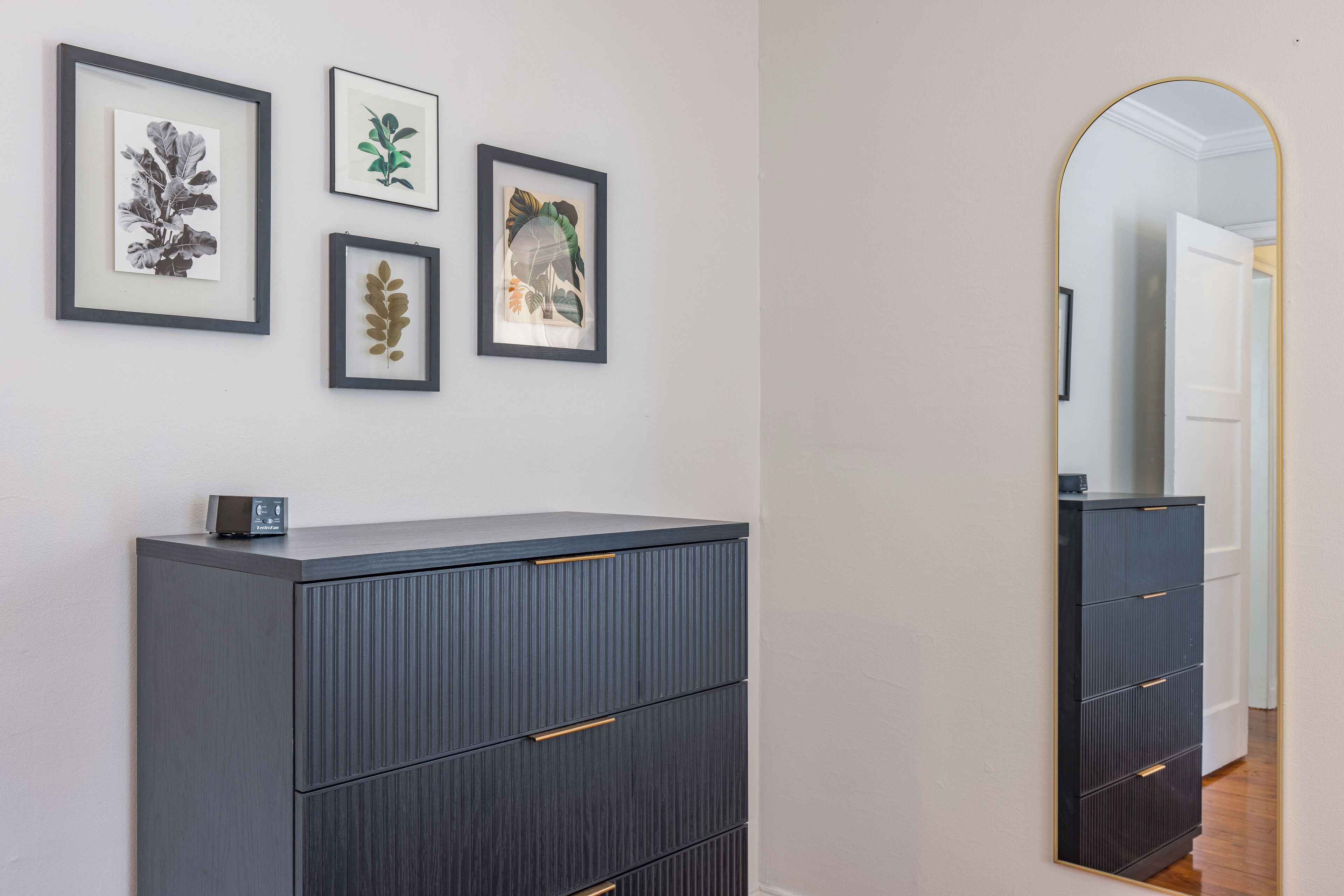 Een moderne kamer met een grijs kastje, een spiegel en drie ingelijste botanische prints aan de muur.