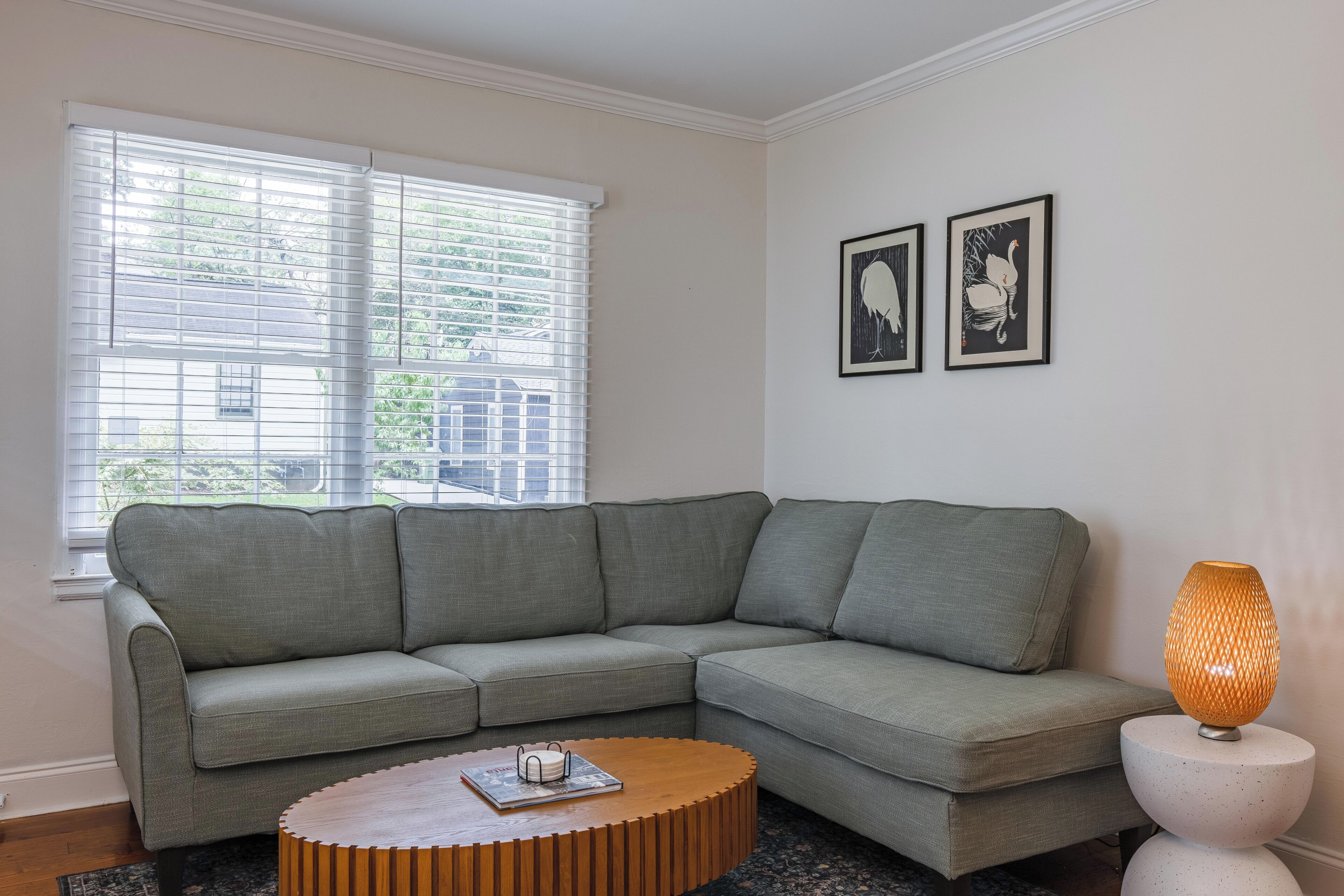 Un salon moderne avec un canapé d’angle, une table basse ronde, un lampadaire et deux œuvres d’art encadrées accrochées au mur.