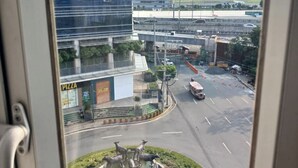 Uitzicht vanuit een raam op een stadsplein met een rotonde, een pizzeria en een modern gebouw.