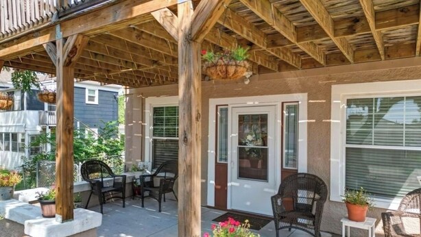 A covered patio area with outdoor furniture, potted plants, and a wooden pergola structure. - The Charming Chestnut (Arkansas City)
