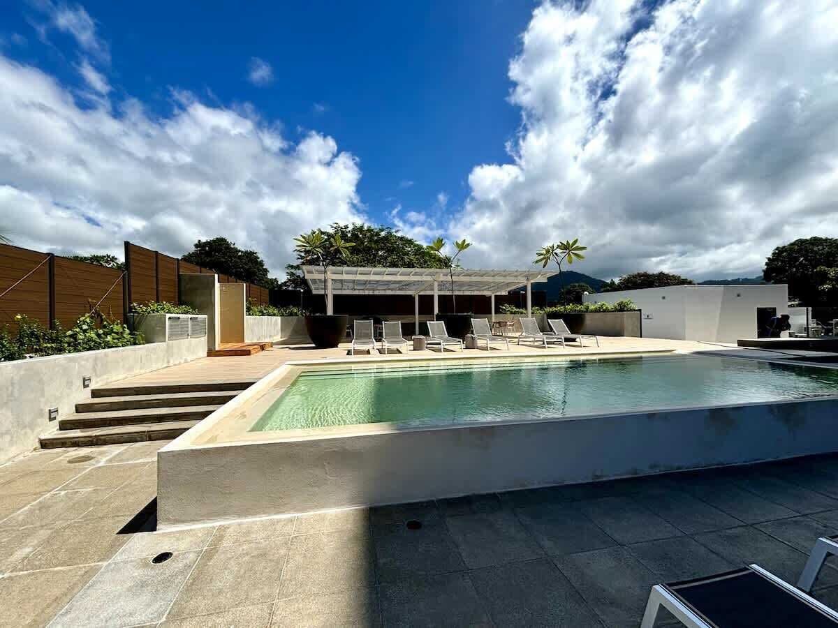 Une piscine dotée de chaises longues, d’une pergola et offrant une vue sur le ciel.