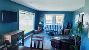 A living room with a blue wall, a striped sofa, a wooden coffee table, a TV, and a window with a view of the outside. - Amazing 2-bedroom house in Astoria (Astoria)