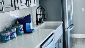 A modern kitchen with grey cabinets, a stainless steel refrigerator, and a dishwasher. There are decorative jars on the counter and a blue coffee maker. - Amazing 2-bedroom house in Astoria (Astoria)