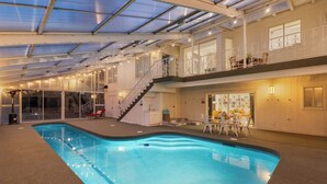Une piscine intérieure dotée d’un toit en verre, d’un escalier et d’un espace repas avec des sièges en plein air.
