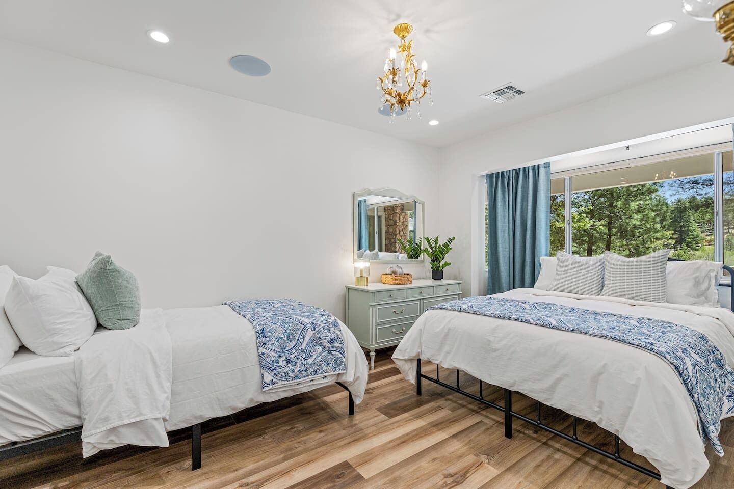 A modern bedroom with two beds, a dresser, a mirror, and a chandelier.