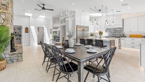 Une cuisine moderne avec des meubles blancs, un îlot central et un coin repas comprenant une grande table et des chaises.
