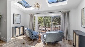 Un salon moderne doté de fenêtres de toit, d’une grande fenêtre et d’un balcon offrant une vue sur les arbres.