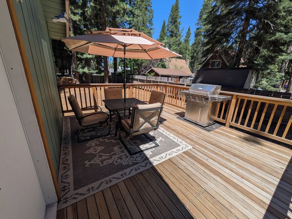A wooden deck with a grill, outdoor furniture, and a patterned rug.