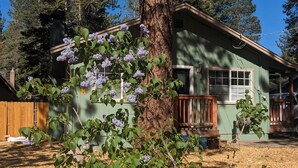 A house with a front porch, a tree with purple flowers, and a clear blue sky. - Cozy South Lake Tahoe Home / Dog Friendly / Fenced Yard / Porch (South Lake Tahoe)