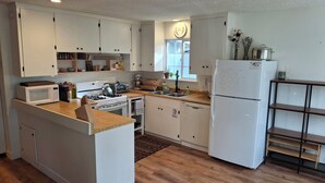 A modern kitchen with white cabinetry, a central island, a built-in oven, a microwave, a toaster, and a refrigerator. - Cozy South Lake Tahoe Home / Dog Friendly / Fenced Yard / Porch (South Lake Tahoe)