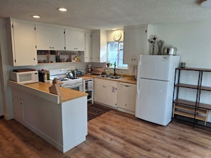 A modern kitchen with white cabinetry, a central island, a built-in oven, a microwave, a toaster, and a refrigerator.