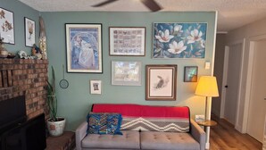 A living room with a fireplace, a sofa with a red cushion, a coffee table, and various framed artworks on the walls. - Cozy South Lake Tahoe Home / Dog Friendly / Fenced Yard / Porch (South Lake Tahoe)