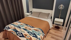 A modern bedroom with a large bed, a bedside table, a floor lamp, and a headboard against a dark wall. - Cozy South Lake Tahoe Home / Dog Friendly / Fenced Yard / Porch (South Lake Tahoe)