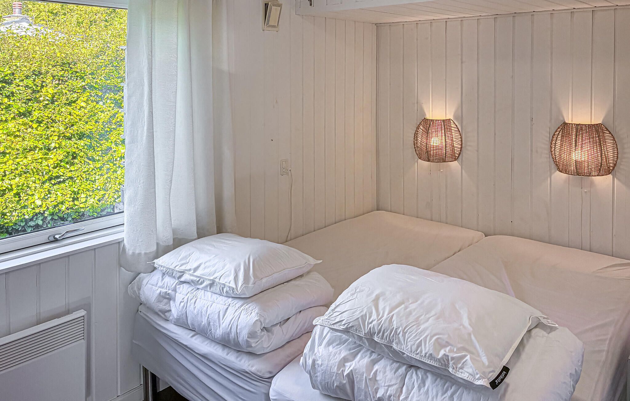 A bedroom with a bed, two bedside tables, a window with curtains, and wall-mounted lights.
