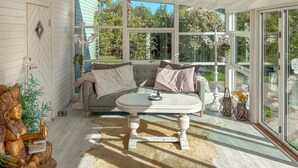 A cozy room with a round table, a cushioned bench, and a large window offering a view of greenery.