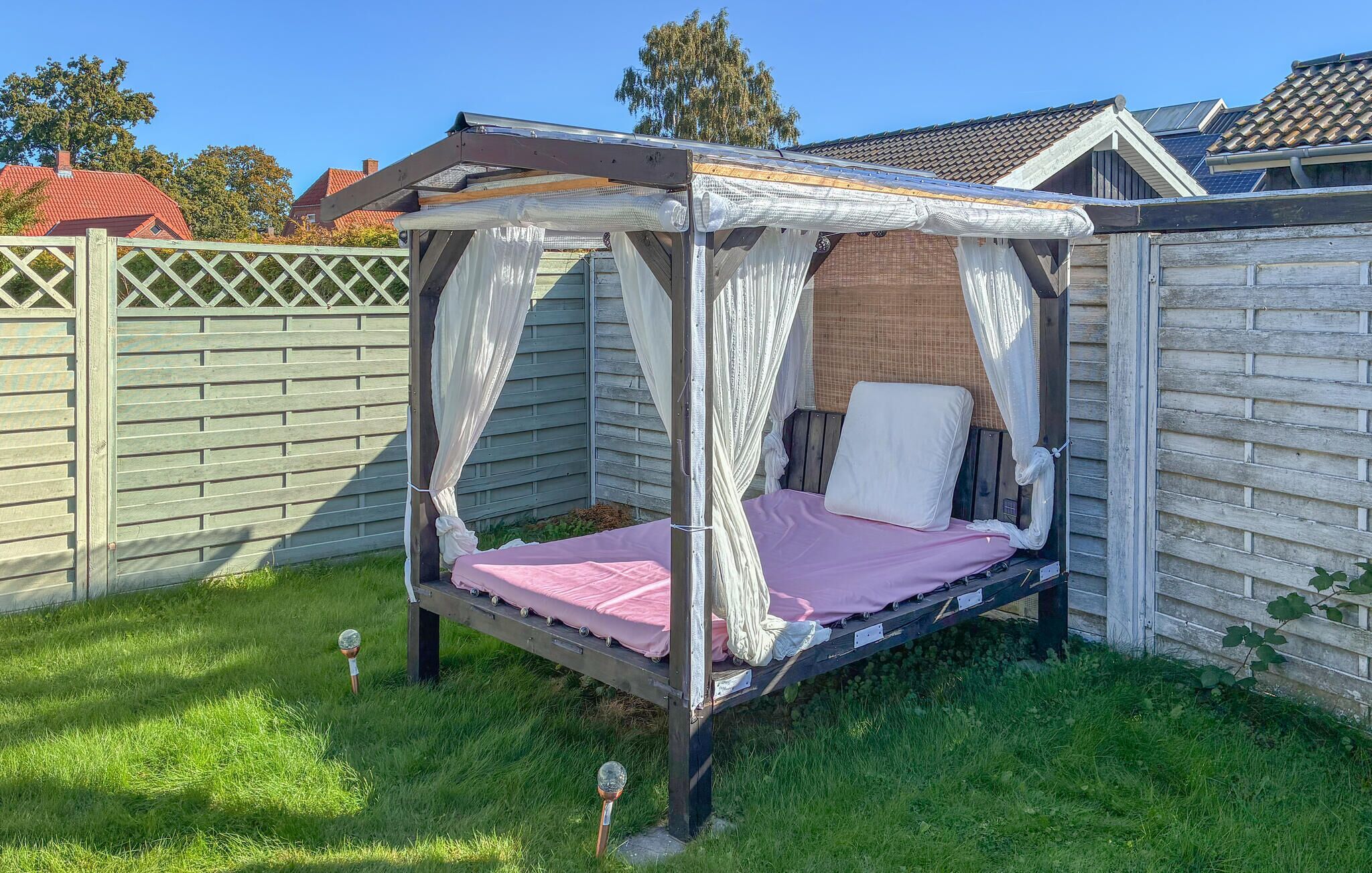 A small, enclosed outdoor bed with a canopy, surrounded by a wooden fence and a grassy area.