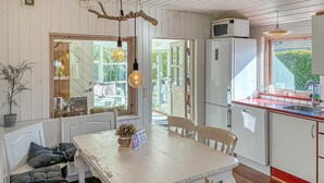 A kitchen with a white table, chairs, and a refrigerator. There is a window with a view of the outside.
