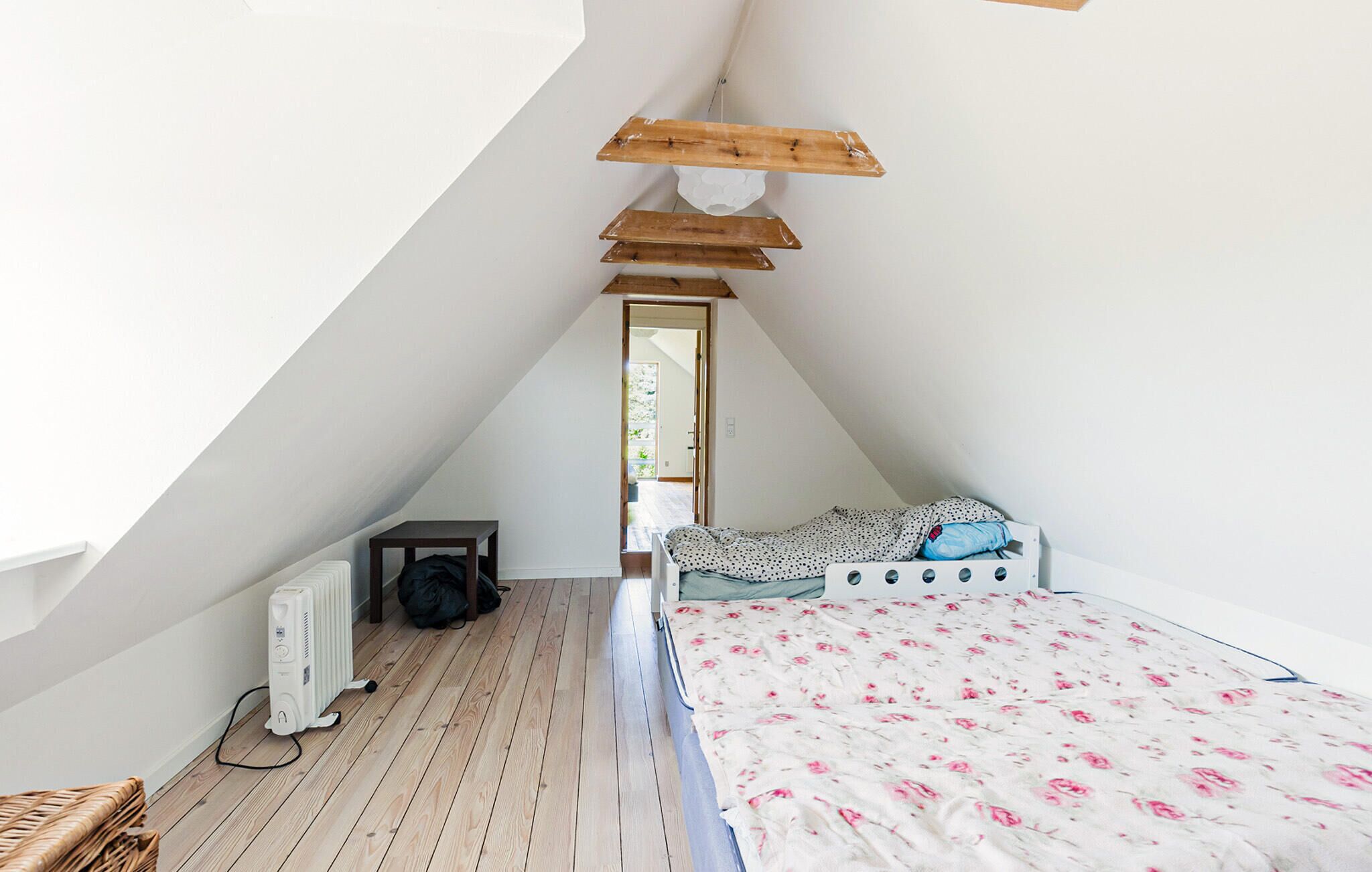 A small, sloped-roofed attic bedroom with a bed, a radiator, and a wooden shelf.