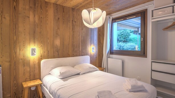 Een opgemaakt bed met witte lakens en handdoeken, een houten wand, en een raam met uitzicht op groen.