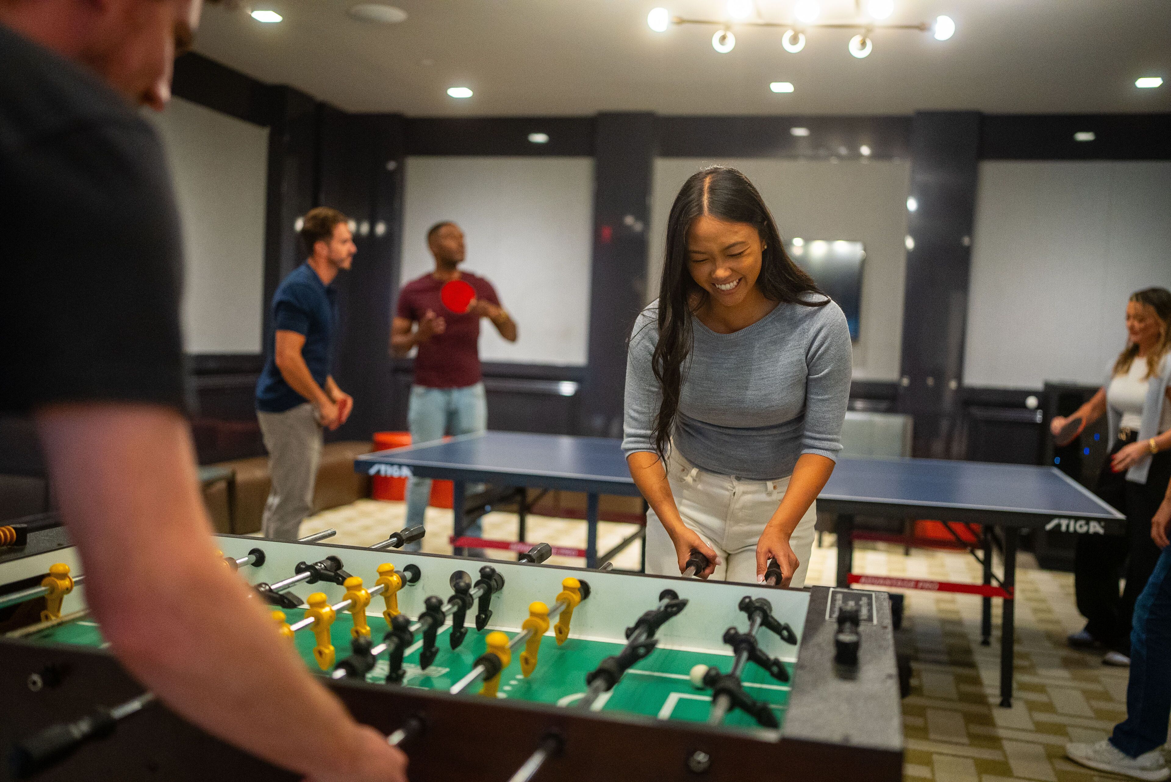 A room with multiple foosball tables and people playing.