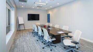 A conference room with a long table, six chairs, a whiteboard, and a TV on the wall.