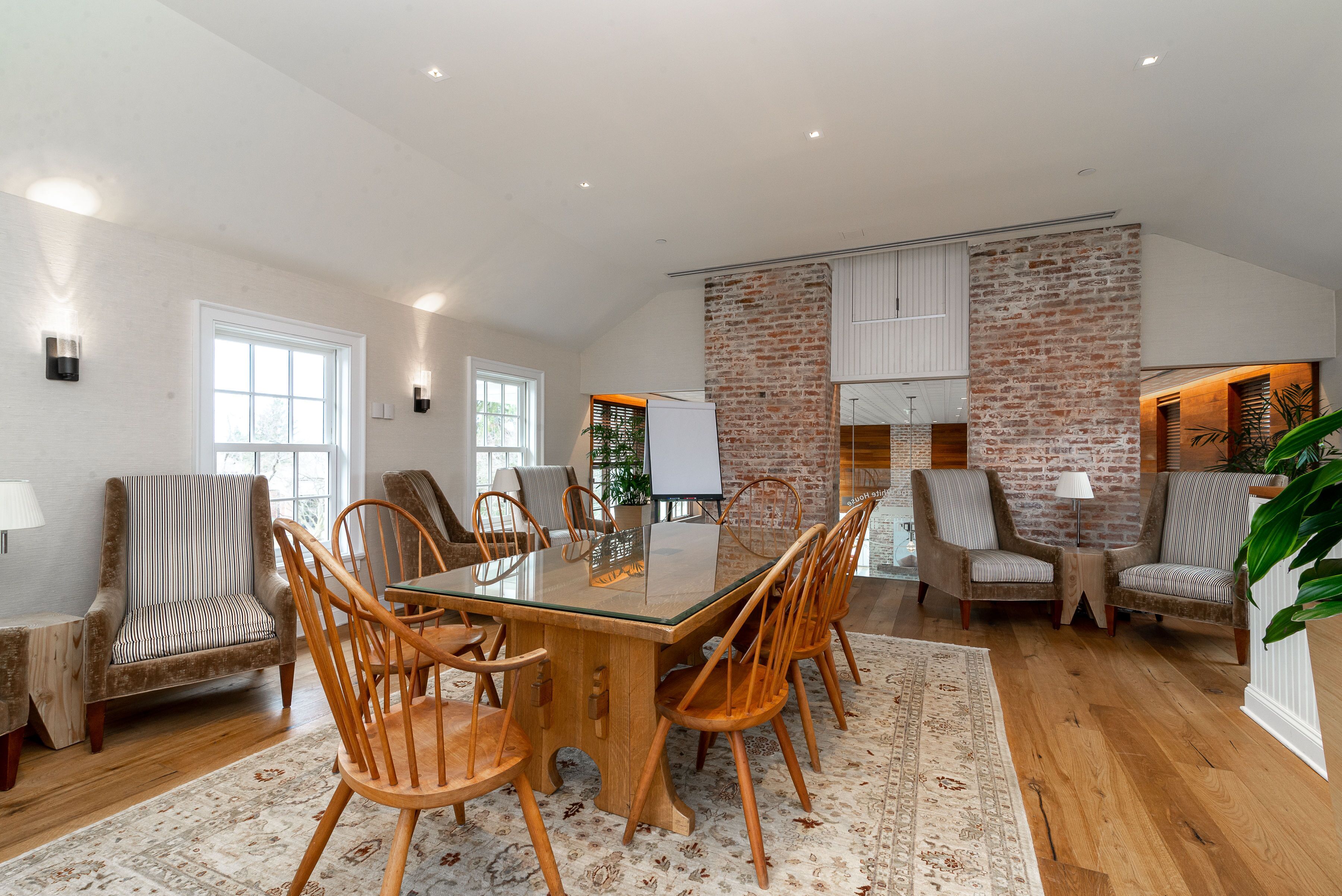 A spacious dining area with a large wooden table and chairs, surrounded by brick walls and large windows.