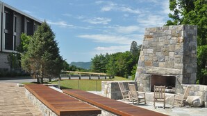 Eine Außenpatio-Terrasse mit einem Steinkamin, Holzmöbeln und Blick auf ein Gebäude im Hintergrund.