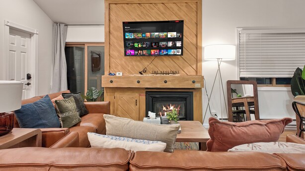Ein Wohnzimmer mit Kamin, einem montierten Fernseher, der Filme anbietet, und einer gemütlichen Sitzecke mit Kissen.