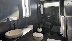 Un bany modern amb un mirall gran, un lavabo rodó, un vàter i una dutxa amb envàs de vidre.