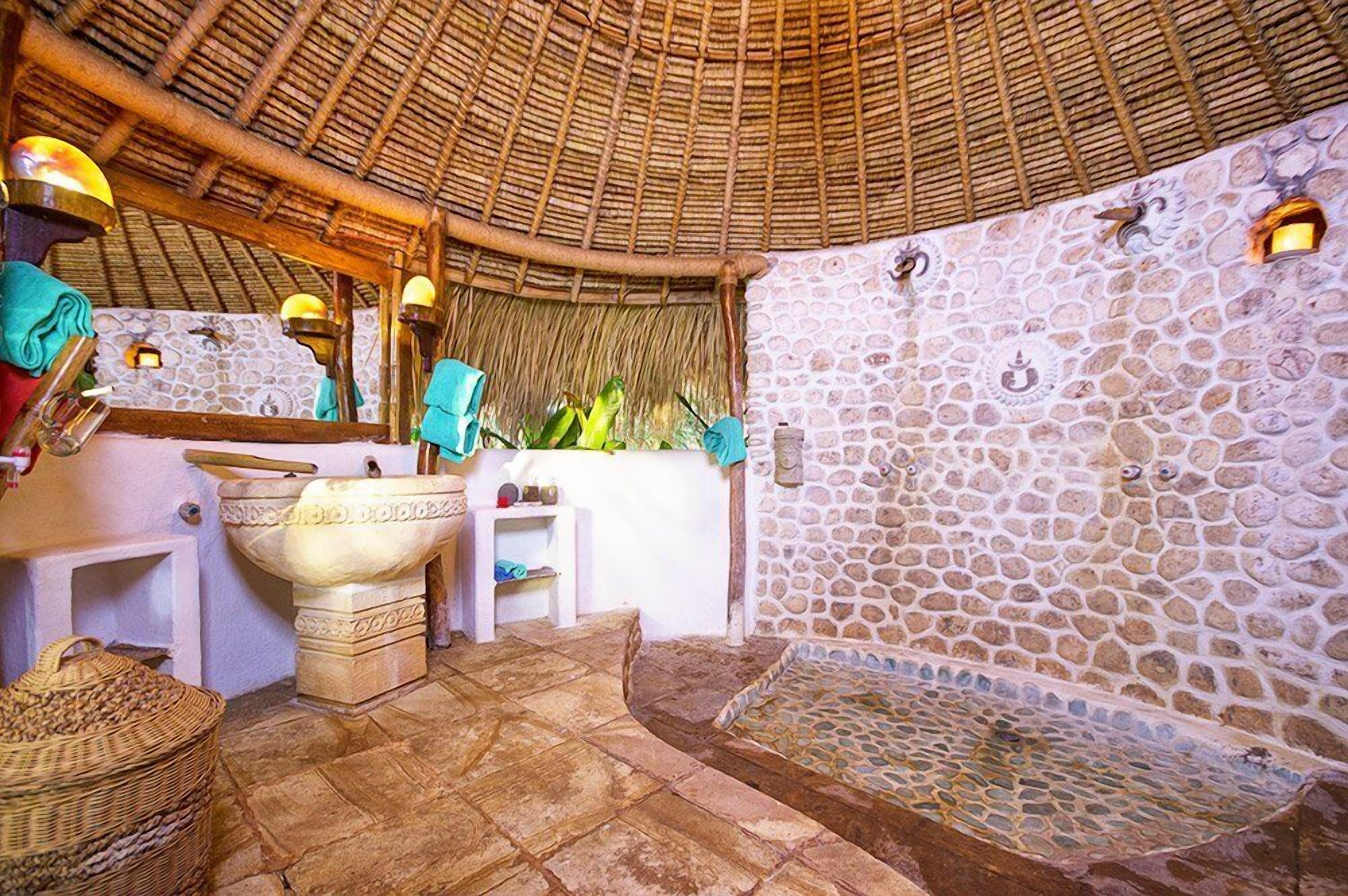 Une salle de bain traditionnelle avec un mur en pierre, un toit de chaume et un lavabo en pierre.