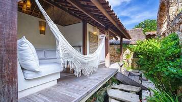 A hammock chair with a cushion, a wooden bench, and a stone wall.