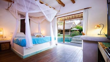 Ein Schlafzimmer mit einem Himmelsbett, ein Pool ist durch eine Glastür sichtbar, und ein kleiner Tisch mit einer Lampe.