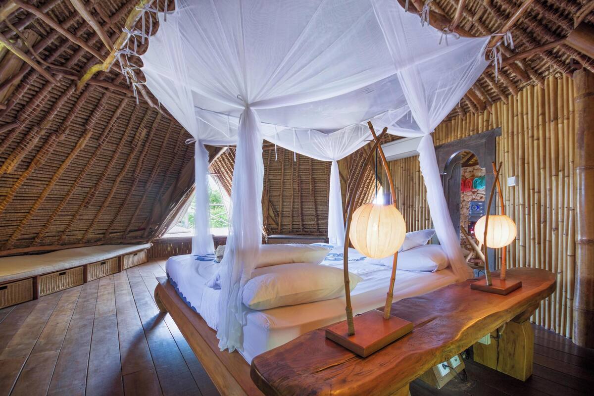 Een kamer met een bed onder een hemelbed, houten vloeren en een bamboevloer.