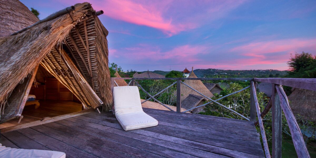 A wooden deck with a thatched-roof structure and a white cushioned chair.