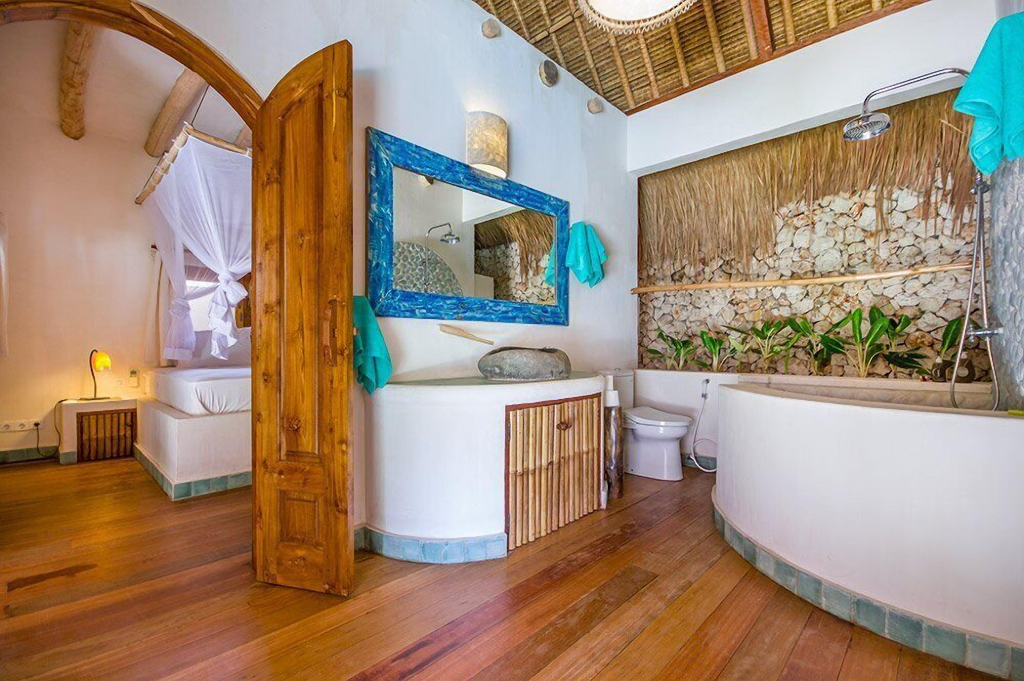 A bathroom with a wooden door, a large mirror, a bathtub, and a shower area.