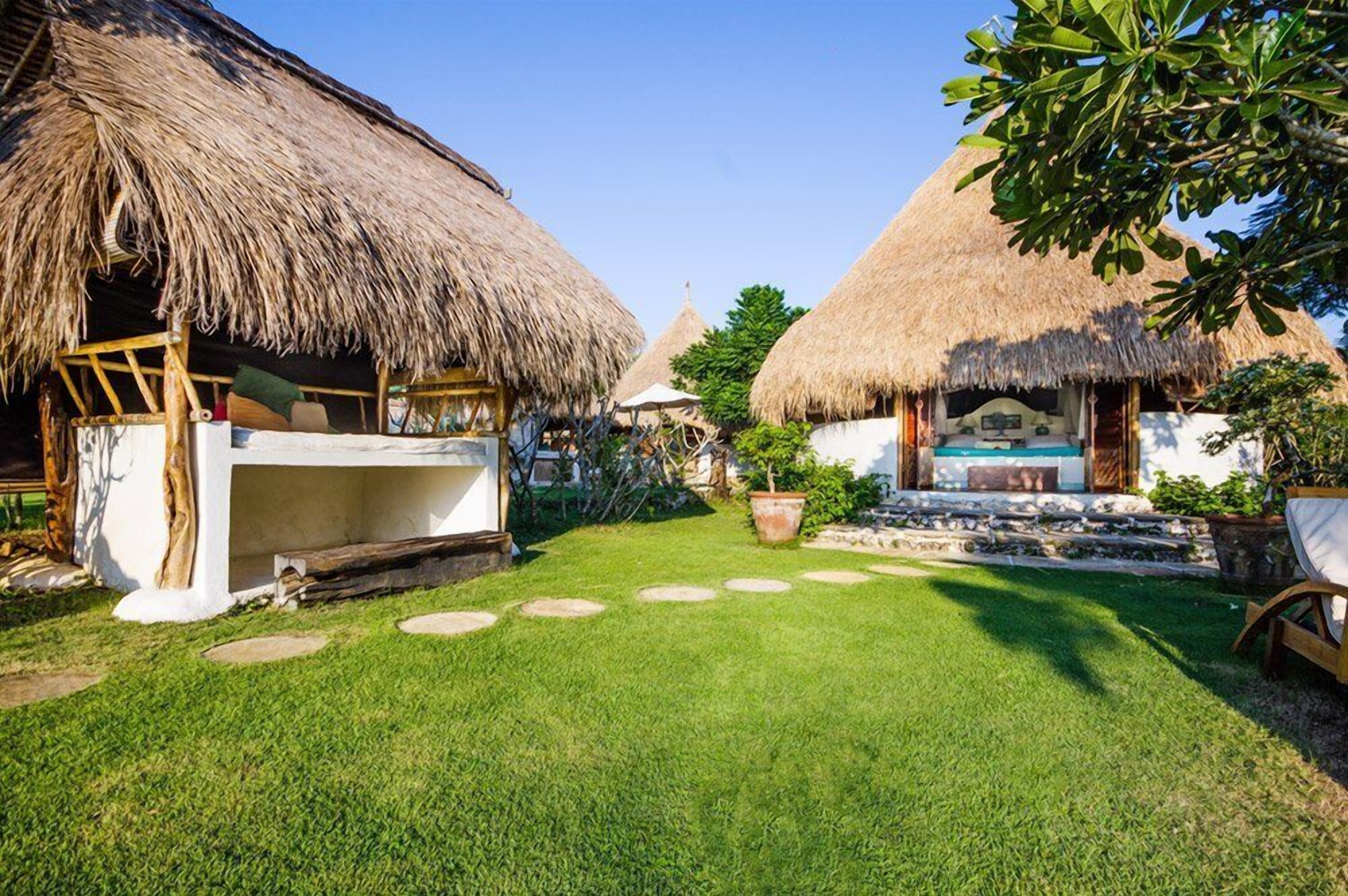 Un complexe hôtelier tropical doté de bungalows aux toits de chaume, d’une piscine et d’une pelouse bien entretenue.