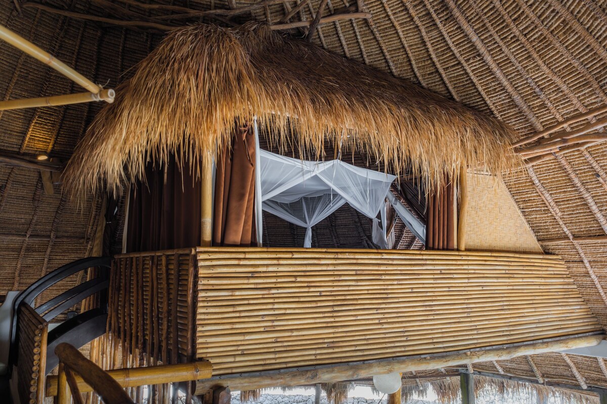 A thatched-roof structure with a wooden platform and a white canopy.