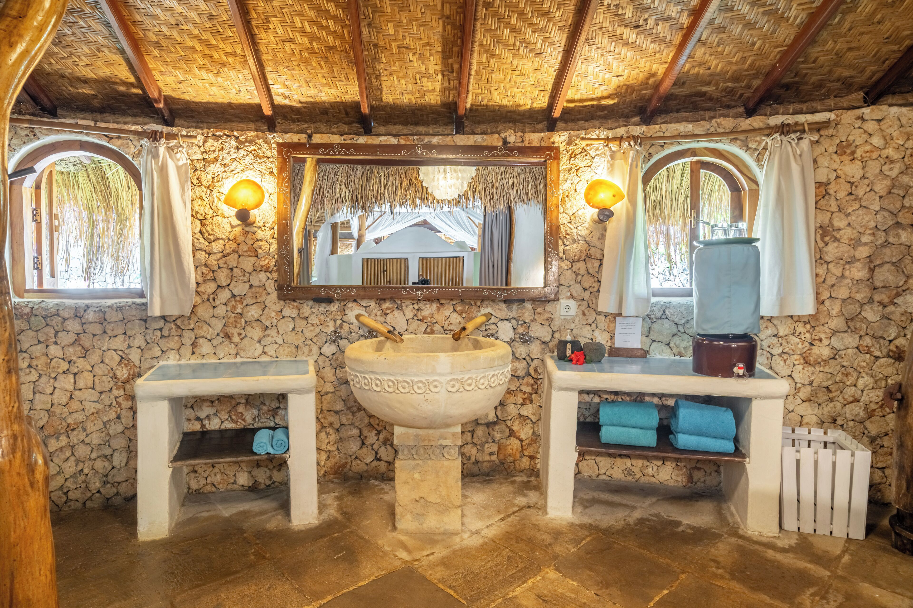 A bathroom with a stone wall, a large basin, two sinks, and a mirror.