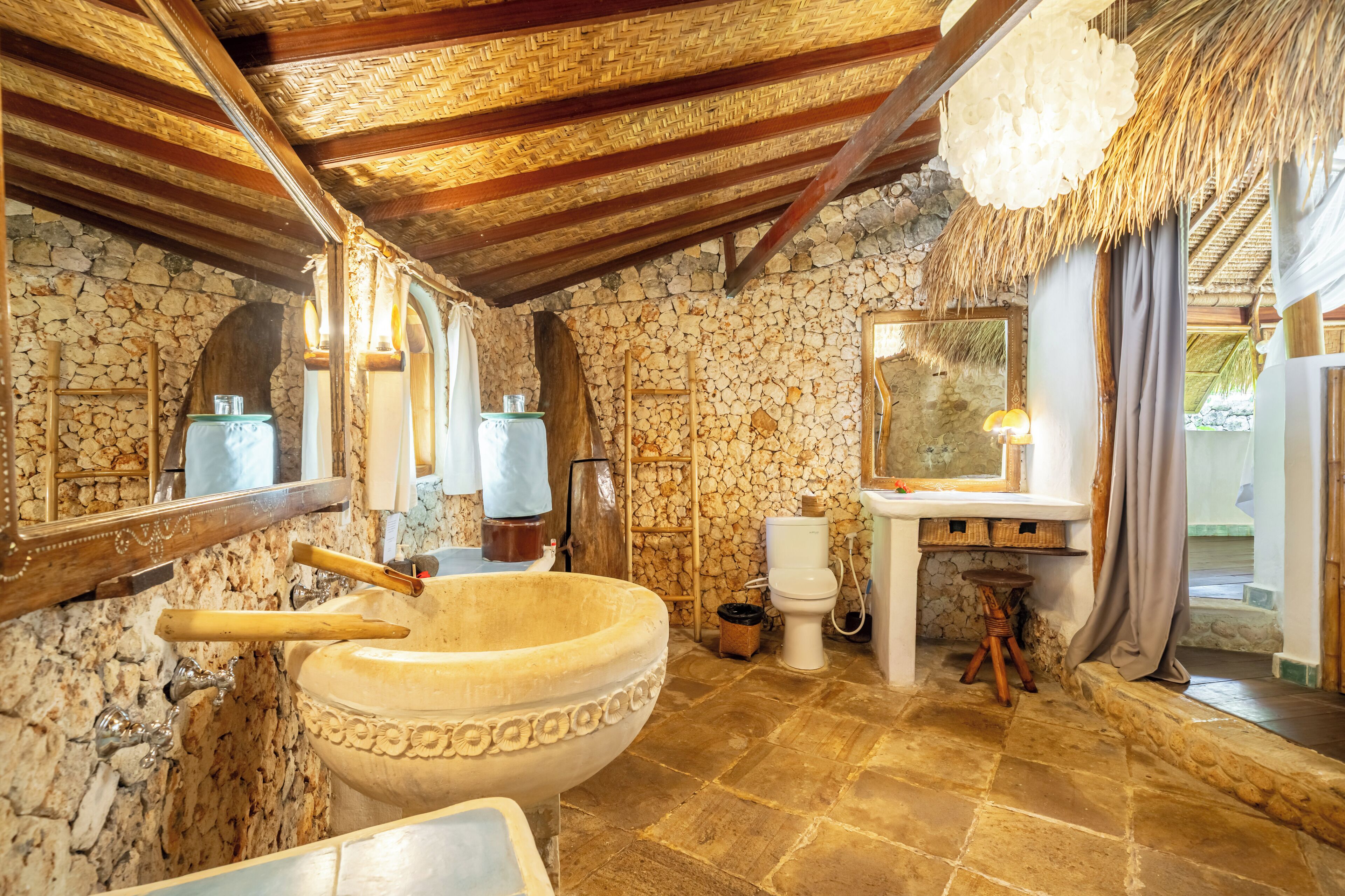 Une salle de bain avec un grand lavabo en pierre, une baignoire en bois et un mur en pierre.
