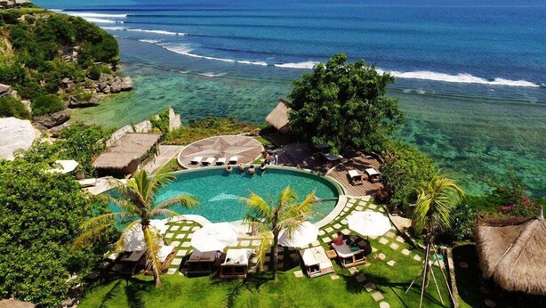Un resort con piscina circondata da poltroncine a sdraio e ombrelloni, con vista sull'oceano cristallino.