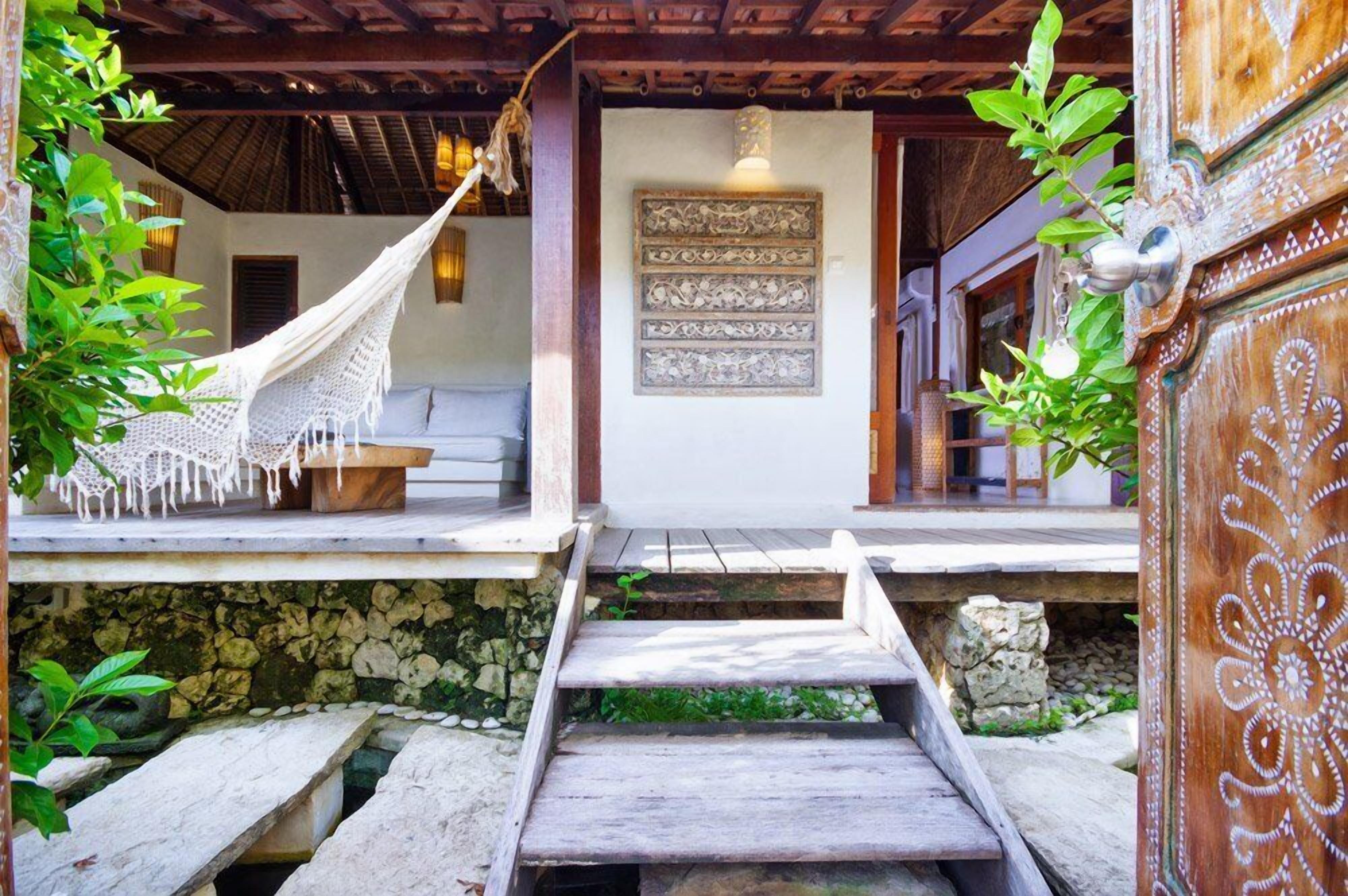 A traditional wooden structure with a hammock, a stone wall, and a wooden door with intricate carvings.