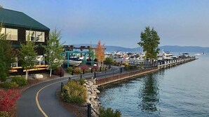 A waterfront walkway with a building on the left, a dock with boats, and a clear view of the water. - Classic Chamberlands Outdoor Living & Soaking Tub! (Homewood)