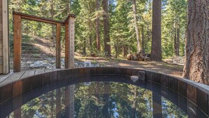 A hot tub in a forested area with wooden structures and a clear view of the surrounding trees. - Classic Chamberlands Outdoor Living & Soaking Tub! (Homewood)