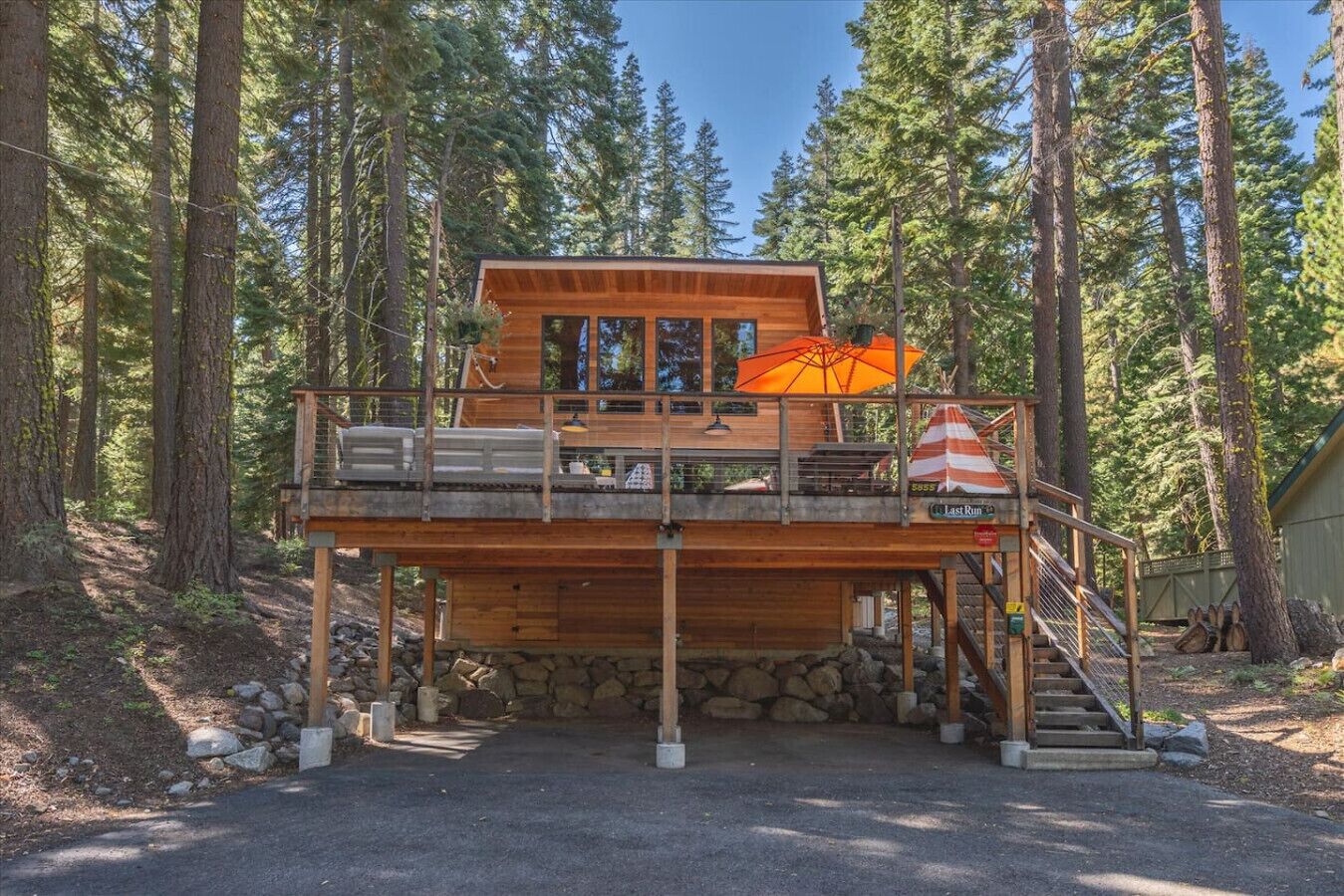 A wooden cabin with a deck, a staircase, and a stone foundation.