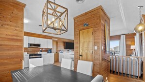 Una cocina moderna con armarios blancos, un comedor con mesa negra y una pared de acento de madera.