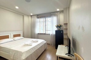 Een hotelkamer met een bed, een bureau, een stoel, een raam met gordijnen en een klein kastje.