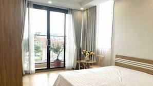 Ein Hotelzimmer mit einem großen Bett, einem kleinen Tisch mit Stühlen, einer Zimmerpflanze und einem Balkon mit Vorhängen.
