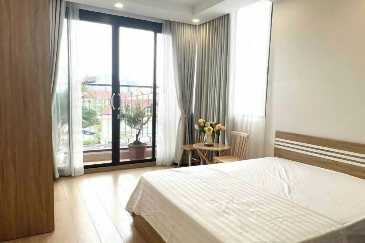 Ein Hotelzimmer mit einem großen Bett, einem kleinen Tisch mit Stühlen, einer Zimmerpflanze und einem Balkon mit Vorhängen.