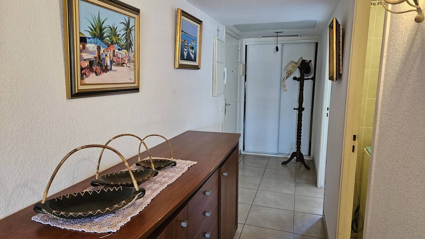 Un couloir avec une commode en bois, deux tableaux encadrés, une porte et une lampe.