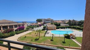A residential area with a swimming pool, a large building with multiple windows, and a clear view of the sea.